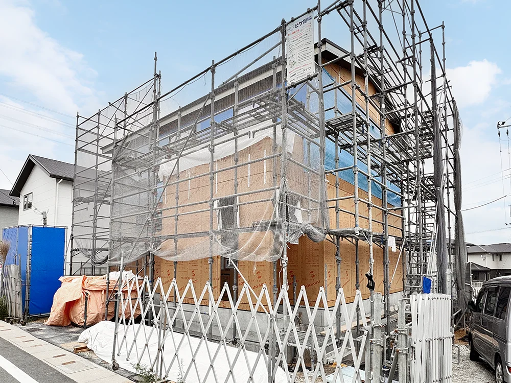 足場に囲まれ外装下地の施工が進む建物の外観