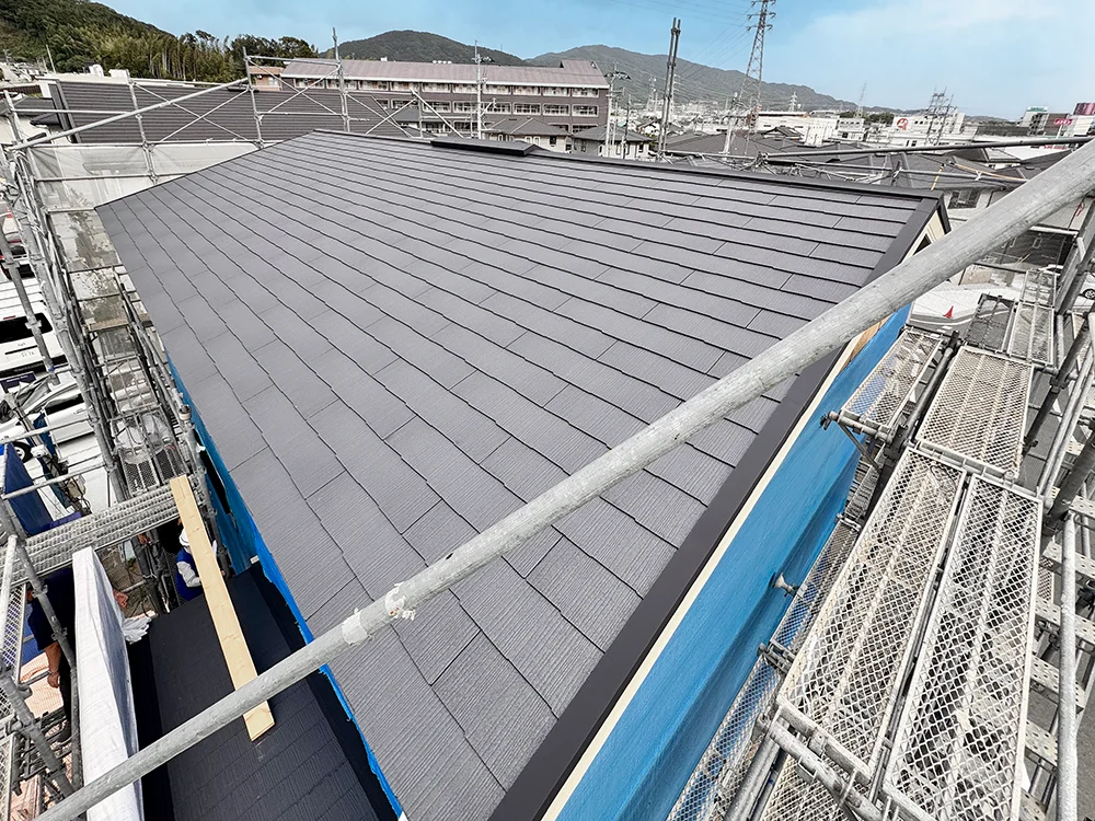 スレート屋根が葺き終わった建物を足場の上から見下ろした様子