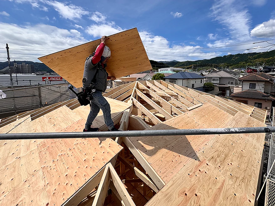 屋根の上で野地板を運搬する職人